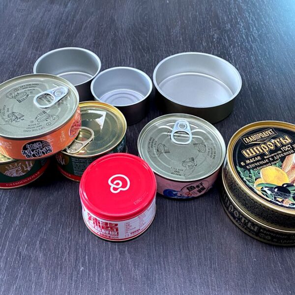 Assortment of metal canned foods on a dark table; several lids removed and pull-tabs visible.