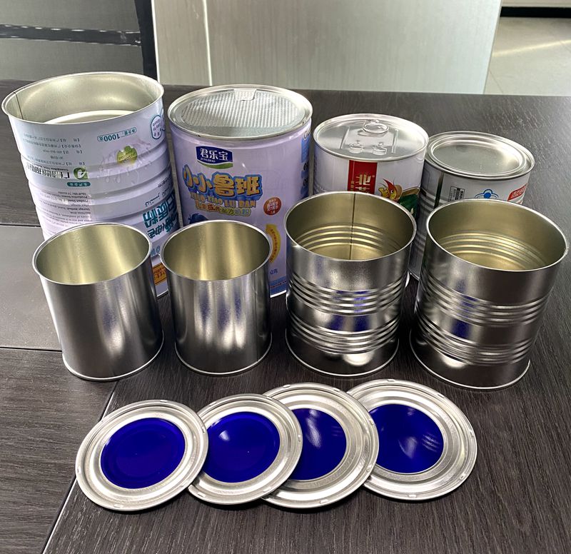 Assorted empty metal cans of varying sizes on a dark surface, with round blue-lidded lids in front.