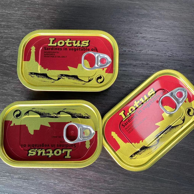 Three yellow-topped sardine tins with red labels reading 'Lotus' placed on a dark wooden surface; each has a pull-tab opening visible.