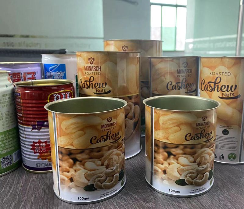 Several metal tins and boxes of Monarch roasted cashew nuts on a countertop shelf.