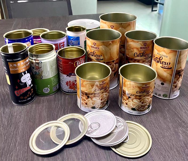 Assortment of cashew-nut tins on a table, mostly Monarch Roasted Cashews, with several open lids and pull rings nearby.
