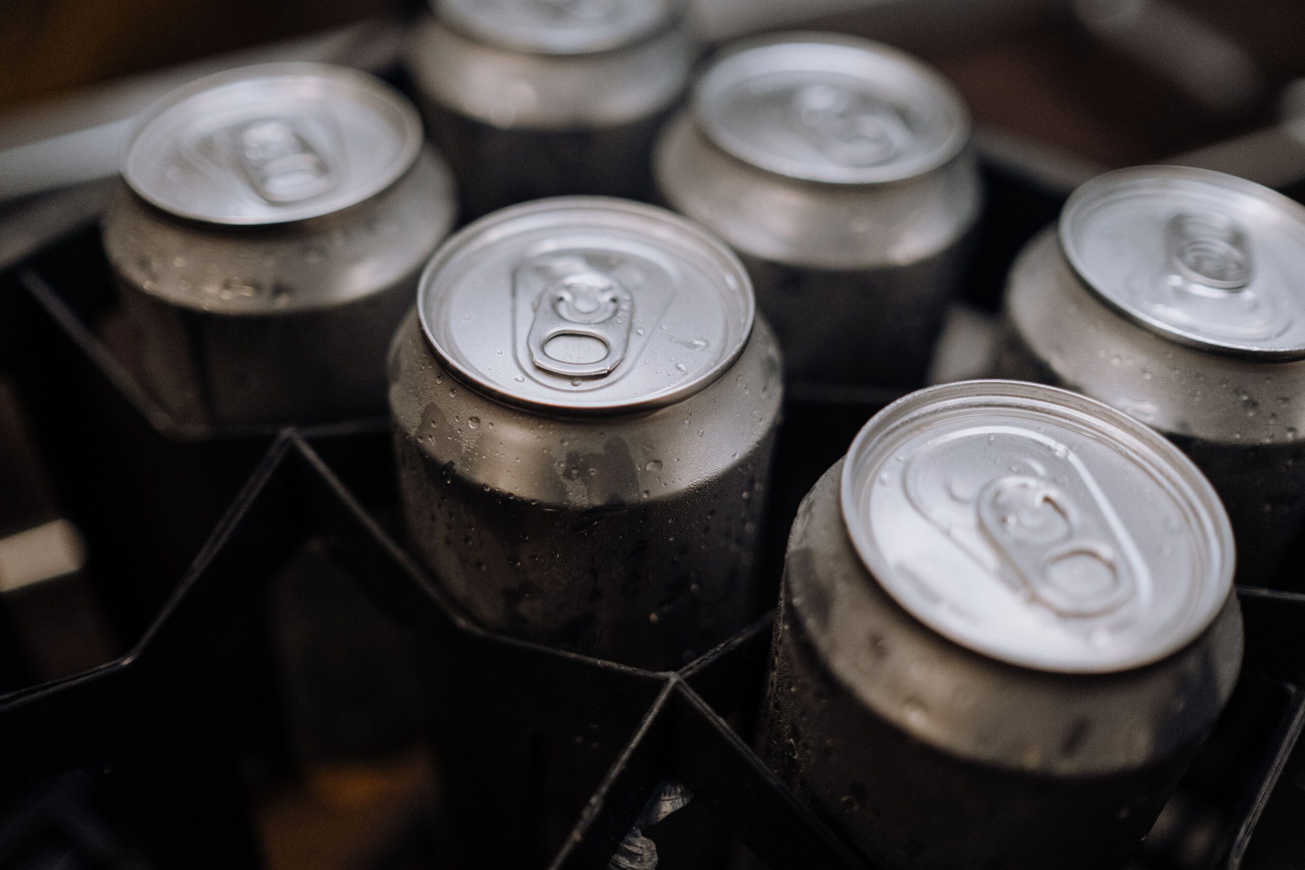 Close-up of aluminum beverage cans with condensation, resting in a dark cooler.